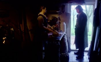 Movie still from “Heart of Glass” (1976), directed by Werner Herzog – Two people standing at a table in front of a door; Wide shot, Over the shoulder angle