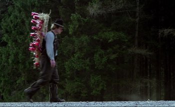 Movie still from “Heart of Glass” (1976), directed by Werner Herzog – A man walking down a road carrying a bunch of fruit; Wide shot, Low angle