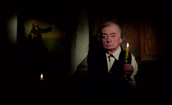 Movie still from “Heart of Glass” (1976), directed by Werner Herzog – An older man holding a candle in a dark room; Medium shot, Low angle