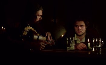 Movie still from “Heart of Glass” (1976), directed by Werner Herzog – Two men sitting at a table with a glass of wine; Medium shot, Low angle