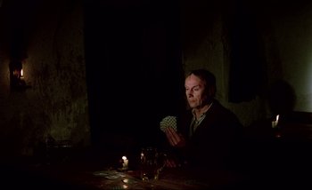 Movie still from “Heart of Glass” (1976), directed by Werner Herzog – A man sitting at a table holding a deck of playing cards; Medium shot, High angle