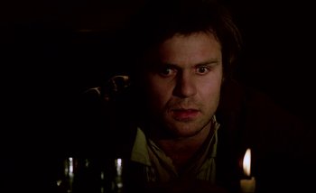 Movie still from “Heart of Glass” (1976), directed by Werner Herzog – A man stares into the camera while sitting in a dimly - lit room; Close Up shot, Low angle