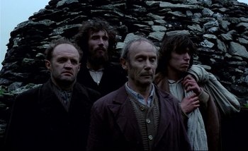 Movie still from “Heart of Glass” (1976), directed by Werner Herzog – A group of men standing next to each other in front of a stone wall; Medium shot, Low angle