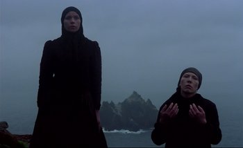 Movie still from “Heart of Glass” (1976), directed by Werner Herzog – Two people standing next to each other near a body of water; Wide shot, Low angle