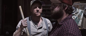 Movie still from “Tucker and Dale vs Evil” (2010), directed by Eli Craig – A man holding a baseball bat next to another man wearing a hat; Medium shot, Over the shoulder angle