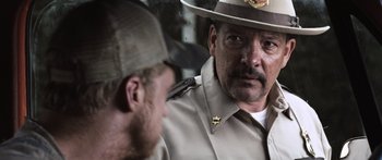 Movie still from “Tucker and Dale vs Evil” (2010), directed by Eli Craig – A man in a sheriff's uniform talking to another man in a hat; Close Up shot, Over the shoulder angle
