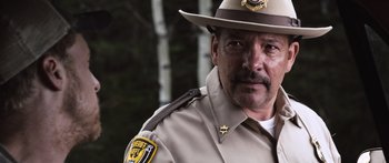 Movie still from “Tucker and Dale vs Evil” (2010), directed by Eli Craig – A man in a sheriff's uniform is looking at the camera; Close Up shot, Over the shoulder angle