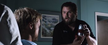 Movie still from “Tucker and Dale vs Evil” (2010), directed by Eli Craig – A man with long hair and a goatee talking to another man in front of a painting; Medium shot, Over the shoulder angle