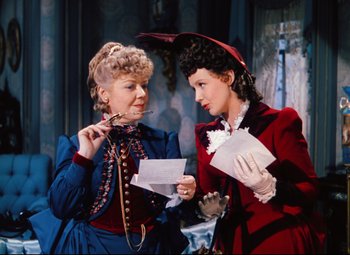 Movie still from “Heaven Can Wait” (1943), directed by Ernst Lubitsch – Two women dressed in period clothing looking at papers; Medium shot, Over the shoulder angle