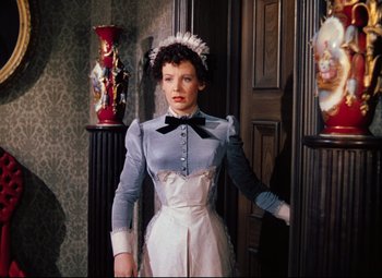 Movie still from “Heaven Can Wait” (1943), directed by Ernst Lubitsch – A woman standing in front of a door wearing a dress and a hat; Medium shot, High angle