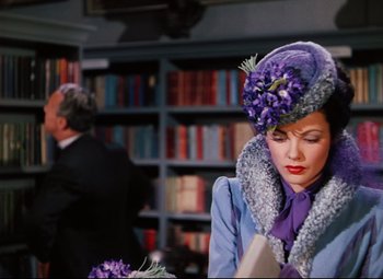 Movie still from “Heaven Can Wait” (1943), directed by Ernst Lubitsch – A woman wearing a purple hat and a purple coat; Medium shot, Over the shoulder angle