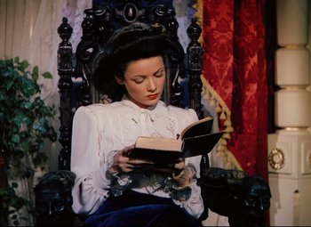 Movie still from “Heaven Can Wait” (1943), directed by Ernst Lubitsch – A woman sitting in a chair reading a book; Medium shot, High angle