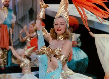 Movie still from “Heaven Can Wait” (1943), directed by Ernst Lubitsch – A woman in a gold costume is holding her hands up; Medium shot, Low angle