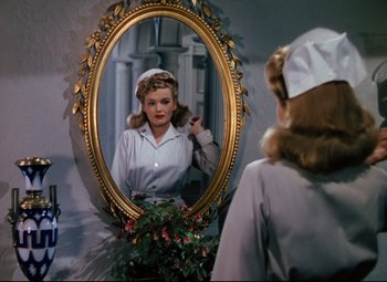 Movie still from “Heaven Can Wait” (1943), directed by Ernst Lubitsch – A woman is looking in the mirror in front of a mirror; Medium shot, Over the shoulder angle