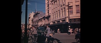 Movie still from “Heavenly Creatures” (1994), directed by Peter Jackson – A group of people riding bikes down a street; Extreme Wide shot, High angle