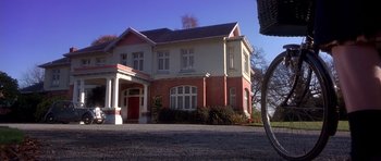 Movie still from “Heavenly Creatures” (1994), directed by Peter Jackson – A red and white two story house sitting on the side of a road; Extreme Wide shot, Low angle