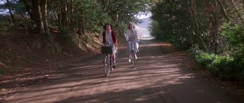Movie still from “Heavenly Creatures” (1994), directed by Peter Jackson – Two women riding bikes down a dirt road; Wide shot, Low angle