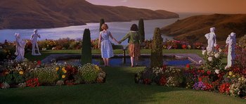 Movie still from “Heavenly Creatures” (1994), directed by Peter Jackson – Two women holding hands in a garden near a lake; Wide shot, High angle