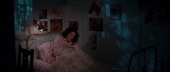 Movie still from “Heavenly Creatures” (1994), directed by Peter Jackson – A woman laying in a bed in a room with pictures on the wall; Medium shot, High angle