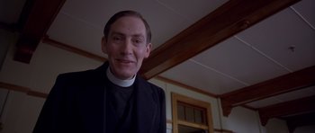 Movie still from “Heavenly Creatures” (1994), directed by Peter Jackson – A man in a priest's outfit smiling for the camera; Close Up shot, Low angle
