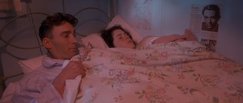 Movie still from “Heavenly Creatures” (1994), directed by Peter Jackson – A man and a woman laying in bed under a blanket; Medium shot, High angle