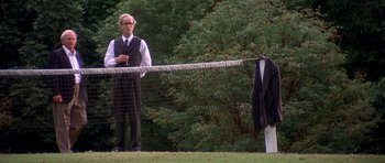 Movie still from “Heavenly Creatures” (1994), directed by Peter Jackson – An older man standing next to a tennis net; Wide shot, Low angle