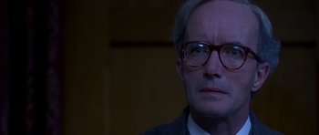 Movie still from “Heavenly Creatures” (1994), directed by Peter Jackson – An older man wearing glasses looking at the camera; Close Up shot, Over the shoulder angle