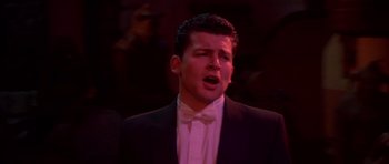 Movie still from “Heavenly Creatures” (1994), directed by Peter Jackson – A man wearing a suit and bow tie singing in front of a crowd; Close Up shot, Low angle