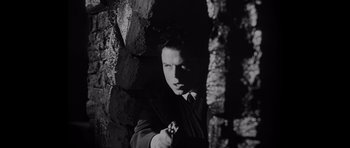 Movie still from “Heavenly Creatures” (1994), directed by Peter Jackson – A black and white photo of a man holding a gun; Medium shot, Low angle