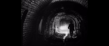 A man is walking through a dark tunnel
