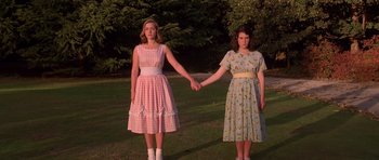 Movie still from “Heavenly Creatures” (1994), directed by Peter Jackson – Two young women holding hands while standing in a field; Medium shot, Low angle