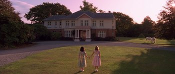 Two young girls holding hands in front of a house
