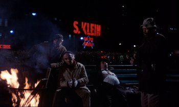 Movie still from “Heavy Traffic” (1973), directed by Ralph Bakshi – A group of people sitting around a fire at a baseball game; Wide shot, Low angle