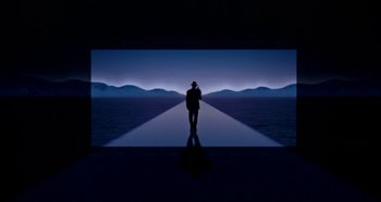 Movie still from “Heavyweights” (1995), directed by Steven Brill – A man standing in front of a screen with mountains in the background; Extreme Wide shot, High angle