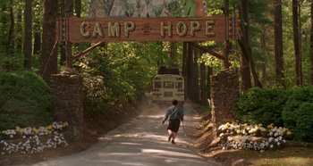 Movie still from “Heavyweights” (1995), directed by Steven Brill – A man walking down a dirt road under a camp hope sign; Extreme Wide shot, Low angle