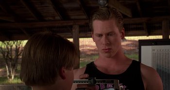 Movie still from “Heavyweights” (1995), directed by Steven Brill – A young man is measuring his height with a weight scale; Medium shot, Over the shoulder angle