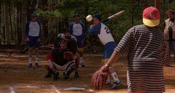 Movie still from “Heavyweights” (1995), directed by Steven Brill – A man swinging a baseball bat at a ball; Medium shot, Over the shoulder angle