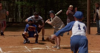 Movie still from “Heavyweights” (1995), directed by Steven Brill – A man swinging a baseball bat on a field; Wide shot, High angle