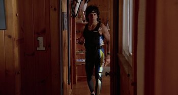 Movie still from “Heavyweights” (1995), directed by Steven Brill – A man in a black and blue outfit standing in a room; Wide shot, Low angle