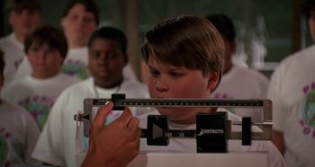 Movie still from “Heavyweights” (1995), directed by Steven Brill – A young boy measuring his height on a scale; Close Up shot, Over the shoulder angle