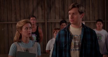 Movie still from “Heavyweights” (1995), directed by Steven Brill – A man and a woman standing next to each other in front of other people; Medium shot, Over the shoulder angle