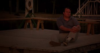 Movie still from “Heavyweights” (1995), directed by Steven Brill – A man sitting on the ground with his legs crossed; Medium shot, High angle