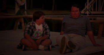 Movie still from “Heavyweights” (1995), directed by Steven Brill – A man and a boy sitting on the ground at night; Medium shot, Over the shoulder angle