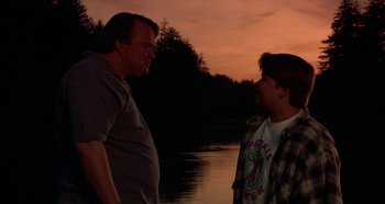 Movie still from “Heavyweights” (1995), directed by Steven Brill – Two men standing next to a body of water at sunset; Medium shot, Over the shoulder angle