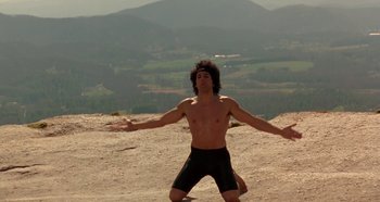 Movie still from “Heavyweights” (1995), directed by Steven Brill – A man standing on top of a hill with his arms outstretched; Wide shot, Low angle