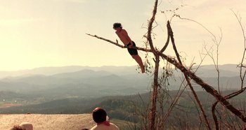 Movie still from “Heavyweights” (1995), directed by Steven Brill – A man is jumping in the air on a tree branch; Wide shot, Low angle