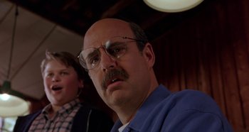 Movie still from “Heavyweights” (1995), directed by Steven Brill – A man with a mustache and glasses is looking at the camera; Close Up shot, Over the shoulder angle