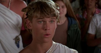 Movie still from “Heavyweights” (1995), directed by Steven Brill – A young man wearing a wreath of leaves in front of other people; Close Up shot, Over the shoulder angle