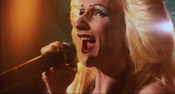Movie still from “Hedwig and the Angry Inch” (2001), directed by John Cameron Mitchell – A woman is holding a microphone up to her mouth; Extreme Close Up shot, Overhead angle