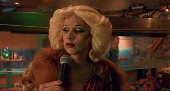 Movie still from “Hedwig and the Angry Inch” (2001), directed by John Cameron Mitchell – A woman with blonde hair and blue eye shadow holding a microphone; Close Up shot, Over the shoulder angle